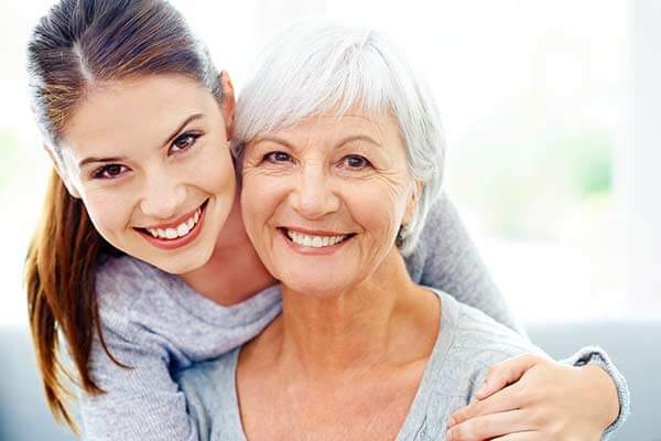 Young adult woman smiling with her arm around her older mother