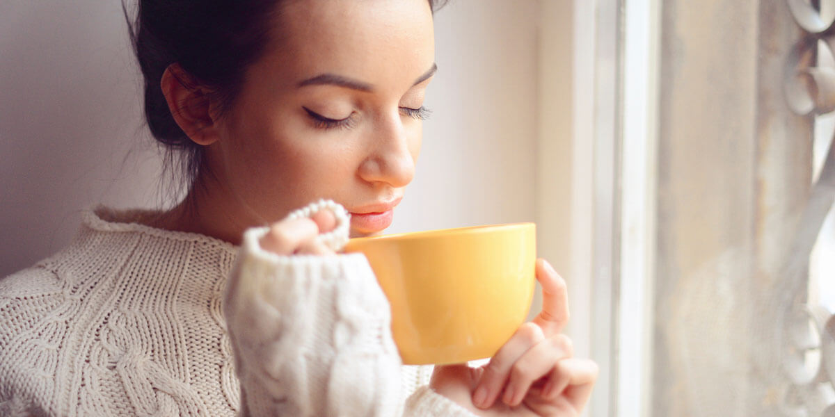 Woman sipping a cup of tea from a yellow mug